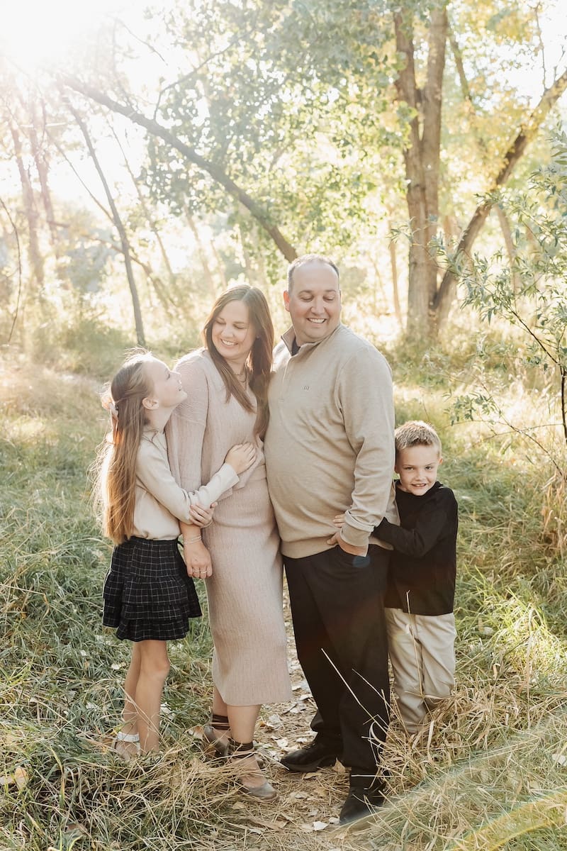A family stands together outdoors near the Jordan River Parkway wearing coordinated neutral-colored outfits.