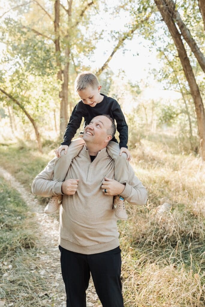 Dad looks up at his young son sitting on his shoulders during their family photo session together.