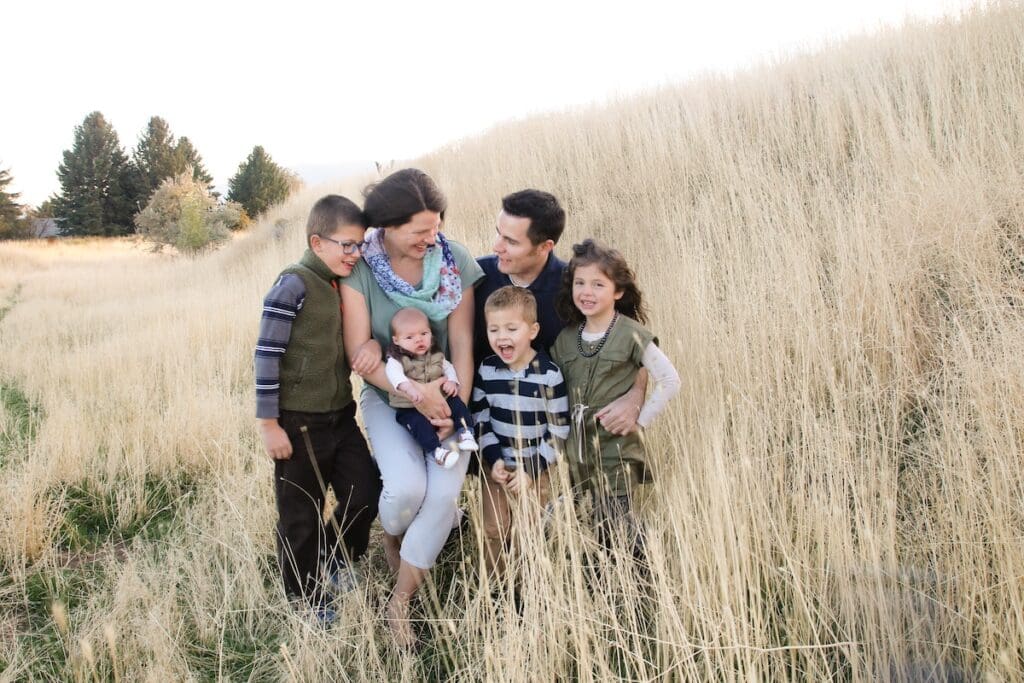 A family snuggles together in a field of tall golden grass wearing army green, gray, and blue during their photo session.