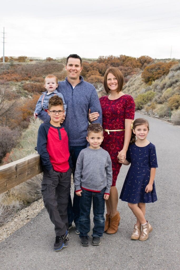 A family of six poses together on a path with autumn foliage in the background in red and navy coordinating clothing.