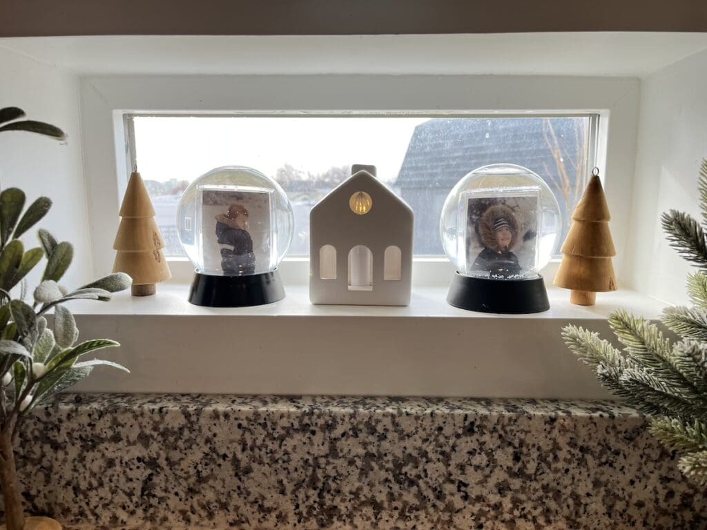 Two photos in snowglobes on a windowsill next to other winter decor.