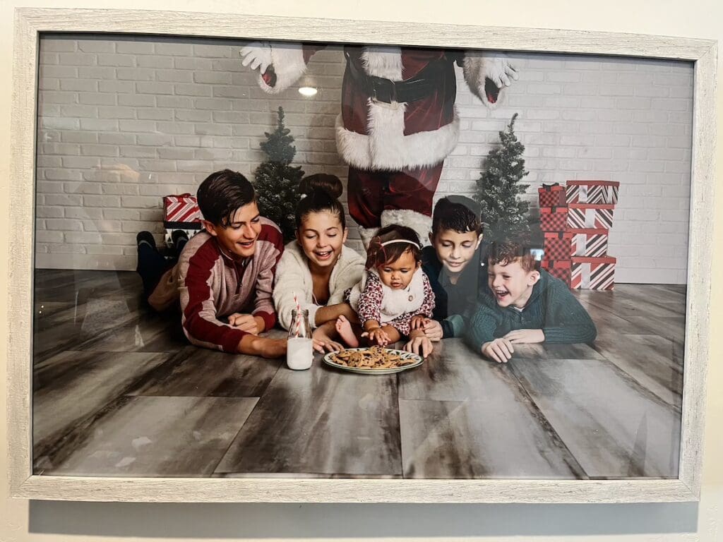 5 children laughing in front of a plate of cookies and glass of milk, meant for Santa, while the youngest reaches to take a cookie.