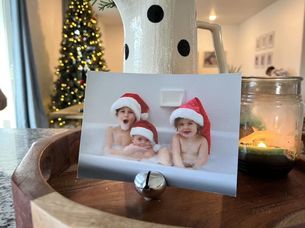 Photo of three young children in a bubble bath, while wearing Santa hats, on display in a little jingle bell.