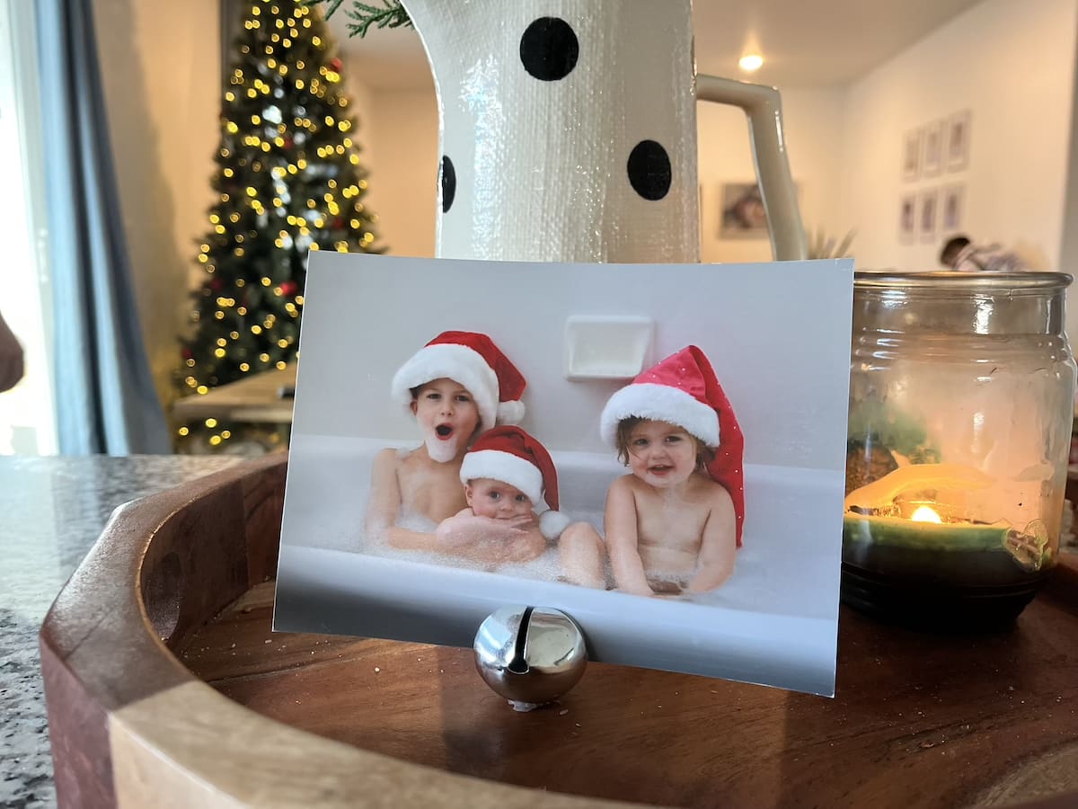 Photo of three young children in a bubble bath, while wearing Santa hats, on display in a little jingle bell.
