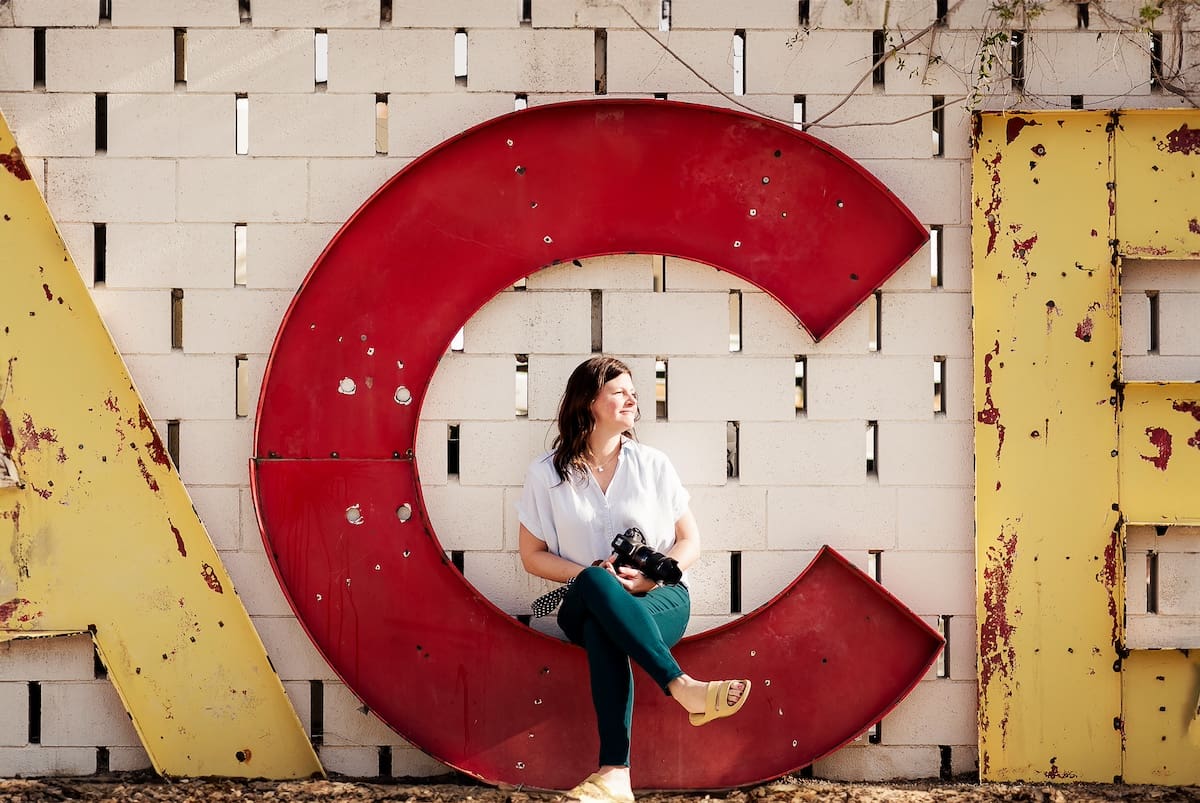Tiffany sits against a wall featuring a large red letter C and partial yellow letters on white brick background.